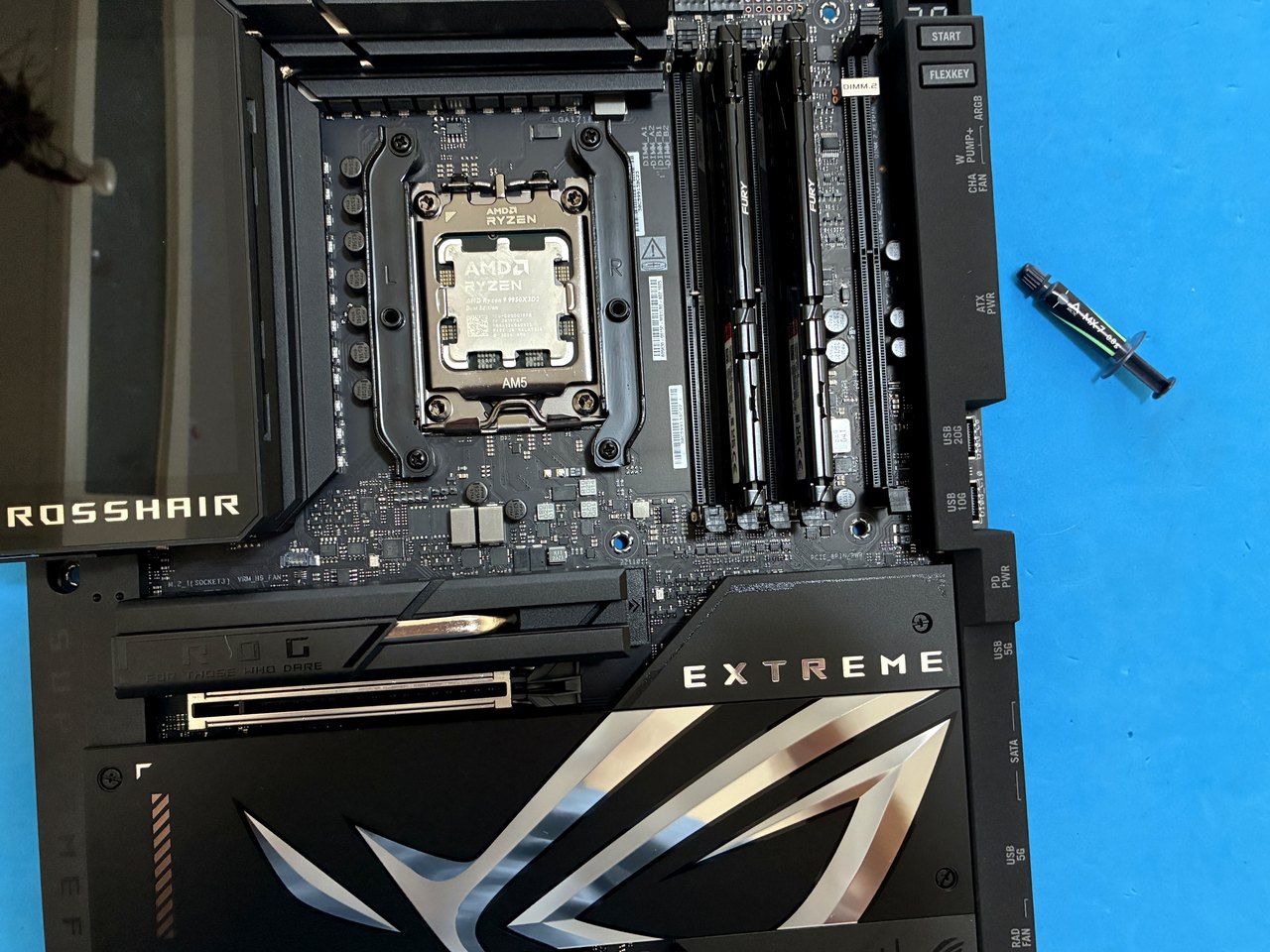 Siringa di pasta termica accanto alla ROG Crosshair Extreme prima del montaggio AIO Arctic